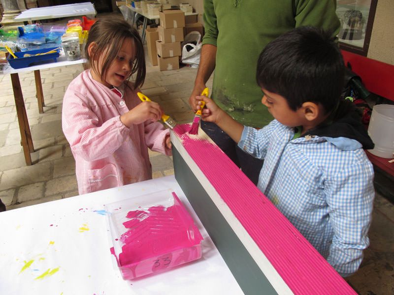  Els nens pinten les peces de fusta del gran joc ELS CONSTRUCTORS_ . El color correspon al color del detall del barri que han triat